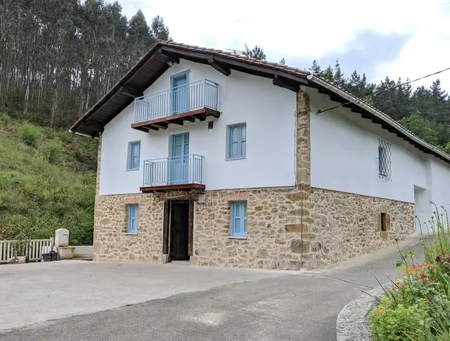Baserri rehabilitado en Larrabetzu con fachada blanca, mampostería de piedra y balcón de madera